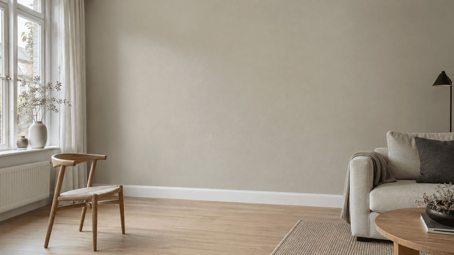 Woonkamer met een warm lichtgrijze wand met beige ondertoon, witte plinten en kozijnen, een eikenhouten vloer, een houten stoel en een lichte bank